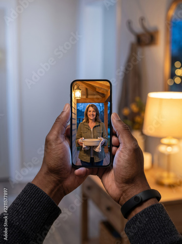 Black man holding an unbranded smartphone showing a neighbor with food, ideal for smart home security and connected community living.