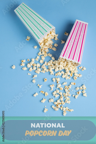 Fresh, tasty popcorn spilling out of colorful striped box containers onto blue background.