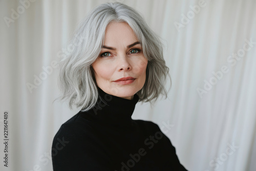 Portrait of a woman with gray hair in a black turtleneck against a soft white background
