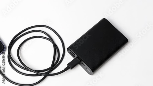 Smartphone connected to a portable power bank with a charging cable on a white background, illustrating mobile charging and backup energy