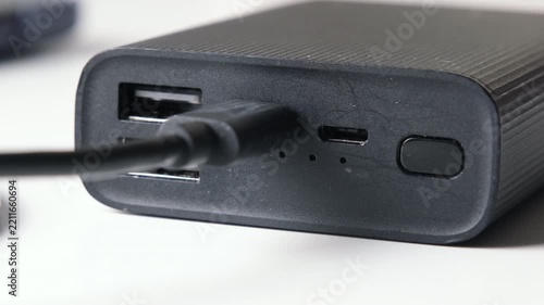 Close-up of a black portable power bank charging through a connected cable, showing usb ports, battery indicator lights and power button on a white background