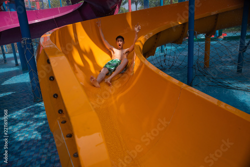 Fotografie Young man having fun on yellow water slide at water park