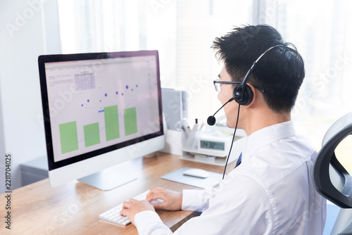 Businessman with Headset Analyzing Financial Data on Computer in Office