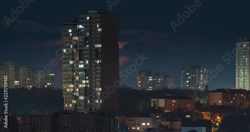 Beautiful dramatic time lapse of a large orange crescent moon setting behind a modern city residential building at night