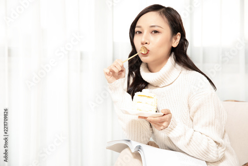 Woman in Cozy Sweater Eating Cake and Reading a Book at Home