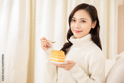 Smiling Woman Holding a Slice of Orange Layered Cake Indoors