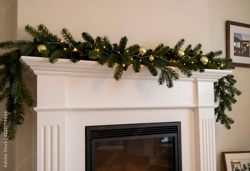 Fototapeta premium Christmas home decor and holiday season celebration, festive fireplace mantel with evergreen pine garland and glowing fairy lights in a cozy living room