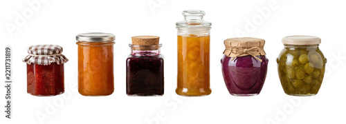 Diverse collection of colorful homemade fruit jams and preserves in assorted glass jars, featuring rustic and traditional canning lids like cork and checkered fabric