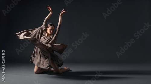 Contemporary dancer performing an expressive full-body movement on a dark studio stage with dramatic lighting, representing dance and performing arts.
