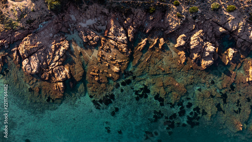 Aerial view of the rugged coastline of Cala Sarraina with jagged rock formations, clear turquoise water, and dark underwater vegetation Trinita d'Agultu e Vignola, Sardinia, Italy.