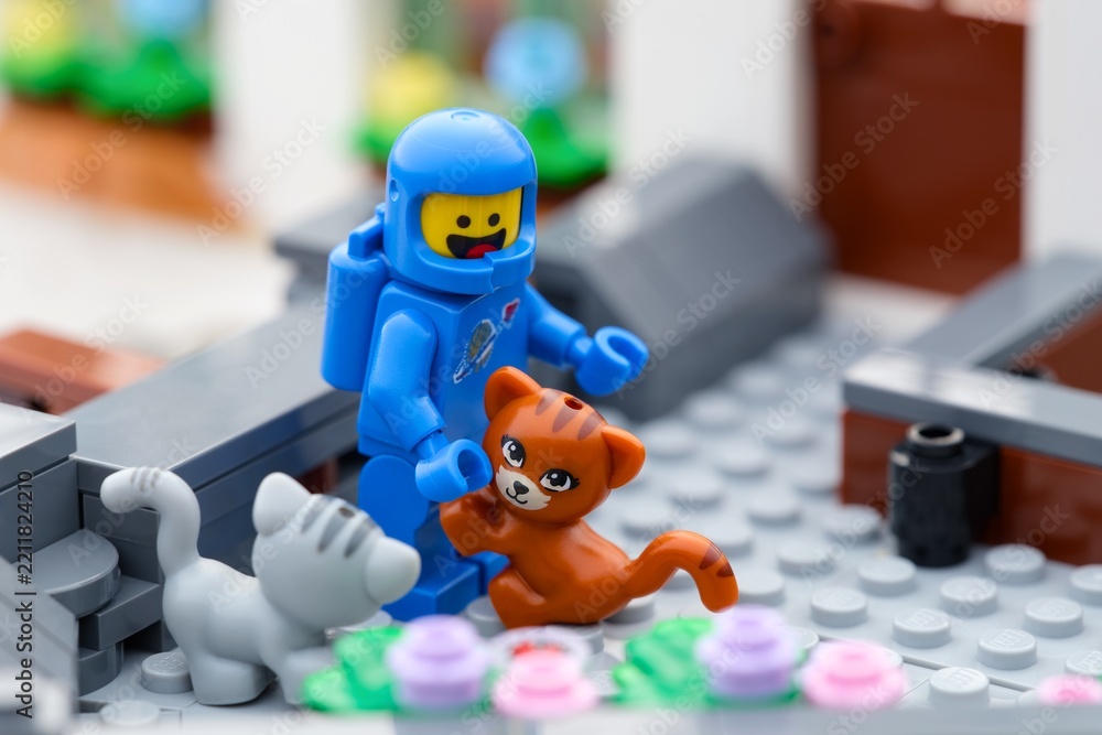 Obraz premium Tambov, Russian Federation - September 24, 2026 A blue Lego astronaut minifigure interactively bends down toward a ginger cat and a gray cat outdoors.