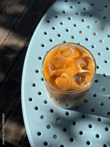 Iced coffee latte with ice cubes in glass on blue perforated metal table in sunny outdoor cafe concept