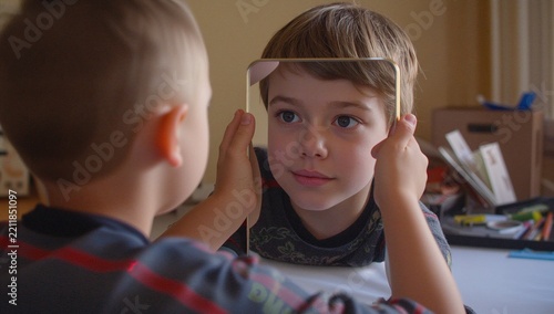 Portrait of Curious Little Boy Looking at His Reflection in Small Handheld Mirror