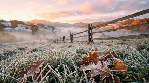 Rural landscape with wooden fence and frosty autumn leaves at sunrise, showing a serene misty valley and distant mountains