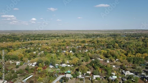 Aerial view of village near lakes in autumn, yellow trees, steppe horizon under clear blue sky. In the distance a body of water, river or lake can be seen.