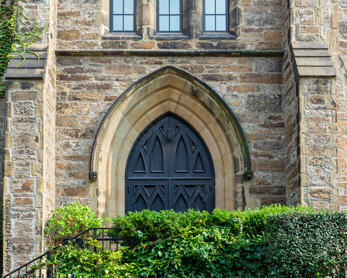 Dark gothic arched door set in a stone masonry wall with green bushes in Boston, South End