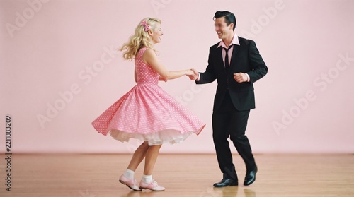 Couple dancing rock and roll in retro style with woman in pink polka dot dress and man in suit