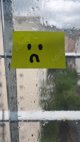 Sad face sticky note on rainy window vertical stuck indoors
