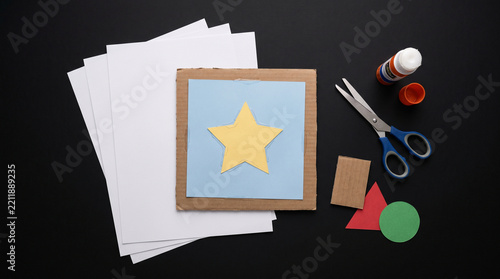 Crafting materials including white paper cardboard glue scissors and colorful paper shapes on black background with crafting supplies with shapes arranged flat