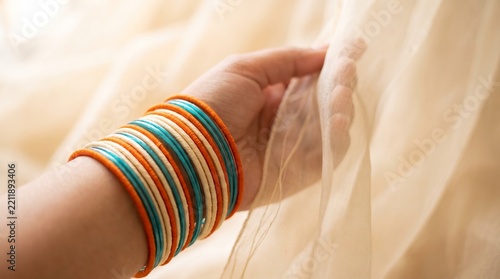 Woman wearing colorful bangles touching a soft silk fabric curtain