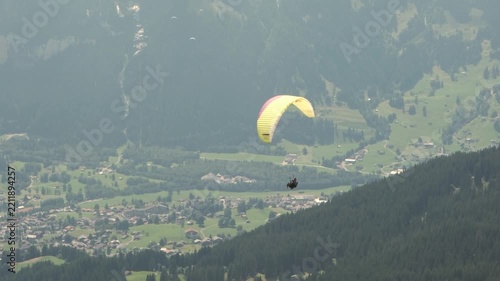 Tandem paragliding flight over a Swiss mountain village, Alps, Switzerland. Professional pilot and passenger flying above scenic alpine landscape. Adventure tourism, outdoor recreation and freedom.