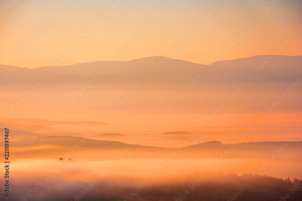 Fototapeta premium cold morning fog with red hot sunrise in the Carpathian mountains. rural valley of Perechyn district in morning mist. nature background with fog rolling over hillls