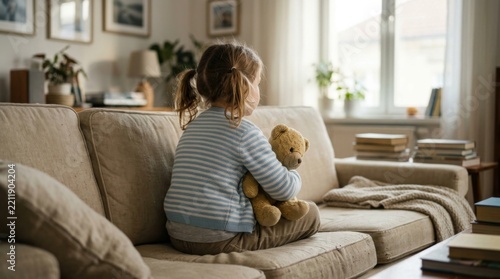 Young girl hugging teddy bear sitting on sofa feeling lonely contemplative mood indoor home interior