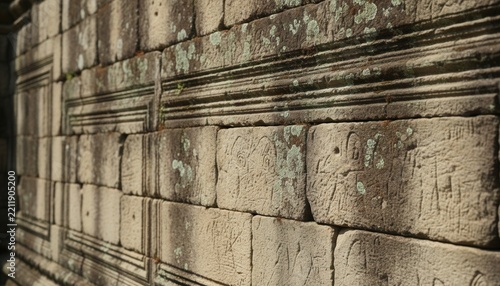 Close up photograph of weathered limestone ashlar masonry blocks on ancient temple wall showing deep grooves and lichen growth
