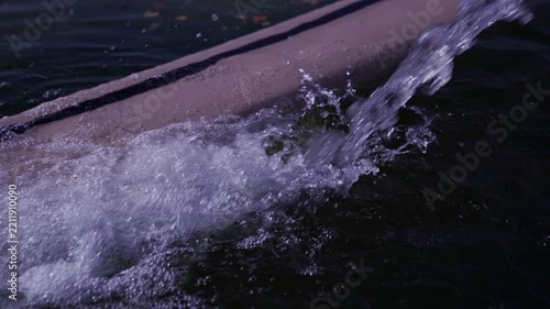 Water jet splashing and flowing into dark water