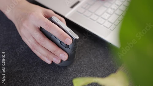Closeup of hand moving and clicking ergonomic vertical mouse beside laptop keyboard. Concept of ergonomic computer accessories and comfortable desk work