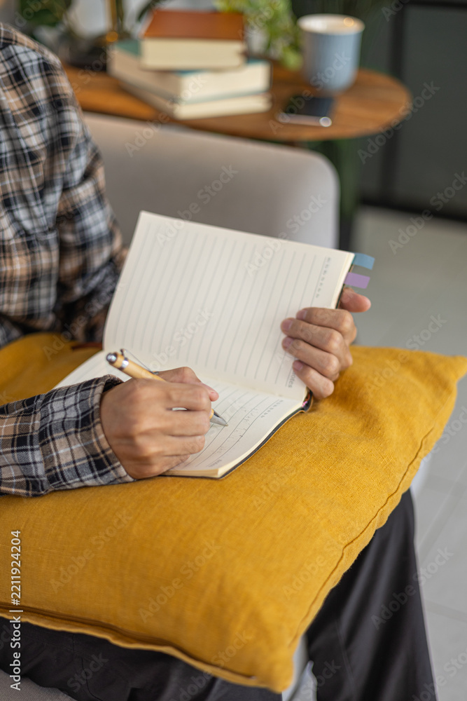 Fototapeta premium Close-up of a man writing in a notebook or journal on a sofa at home.