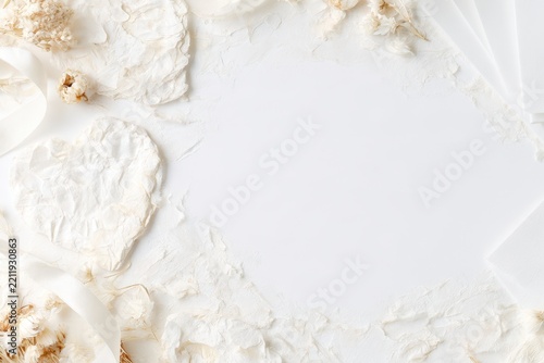 White textured floral paper border with delicate dried flowers and soft fabric folds surrounding a bright central copy space, elegant minimalist background flat lay