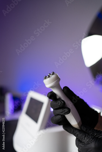 Hand in black glove holding a facial skin rejuvenation device in a beauty clinic