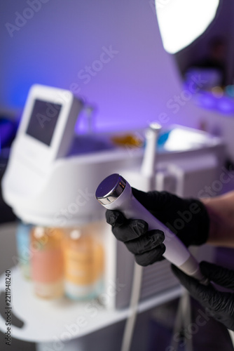Person wearing black gloves holding a cosmetology device for skin care in a salon