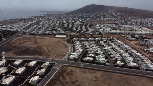 An aerial view of a residential area with a mix of white and brown buildings roads and a large hill in the background