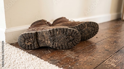 Dirty brown boots leave mud stains on a dark scratched wooden floor.
