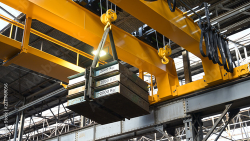 Fotografie Overhead crane lifting heavy steel plates inside a metalworking factory, illustrating heavy industry, material handling, steel production and industrial work