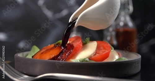 Balsamic vinegar pouring onto caprese salad on black kitchen background slow motion 1000 fps