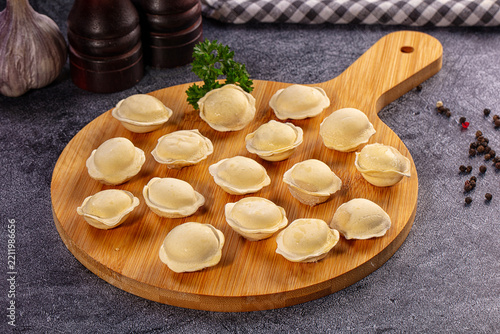 Uncooked dumplings arranged on round wooden cutting board with fresh parsley garnish and scattered peppercorns on dark stone surface