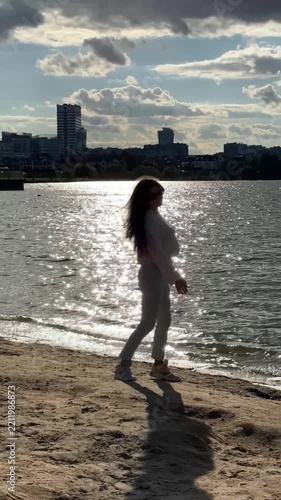 Young Woman In White Sweater Walking On Sandy Beach Against Sunlit Water Video