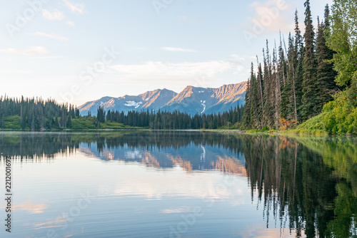 Reflections of mountains in calm lake under blue sky with evergreen trees on sunny day