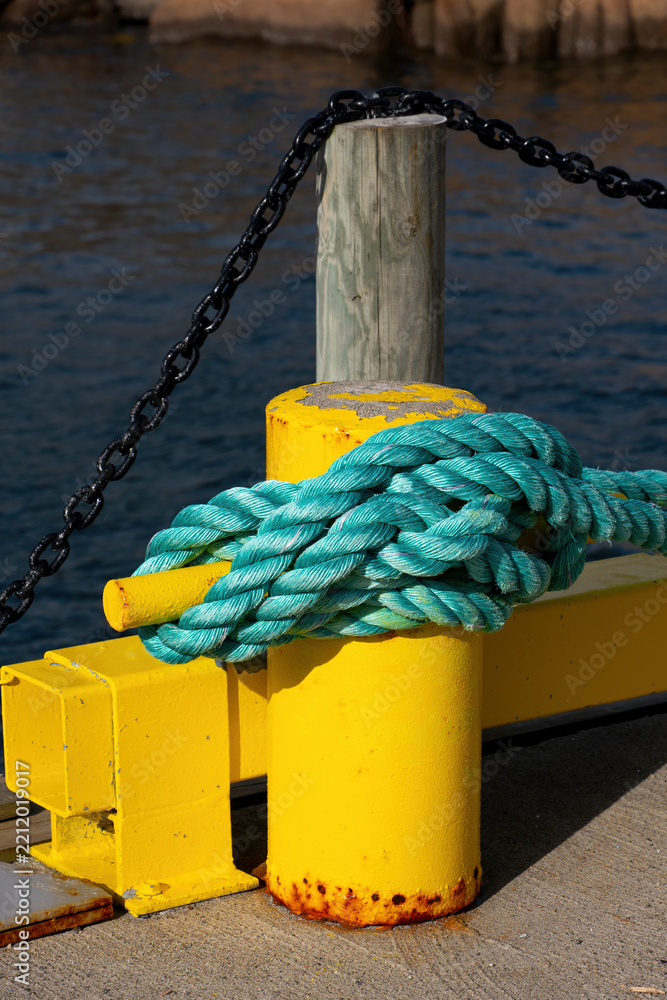 Fototapeta premium Turquoise mooring rope tied around yellow harbor bollard