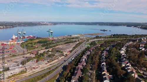 Aerial cinematic shot of a military ship towing another vessel across Halifax Harbour at sunrise, passing under a bridge with the city skyline and waterfront visible beyond.