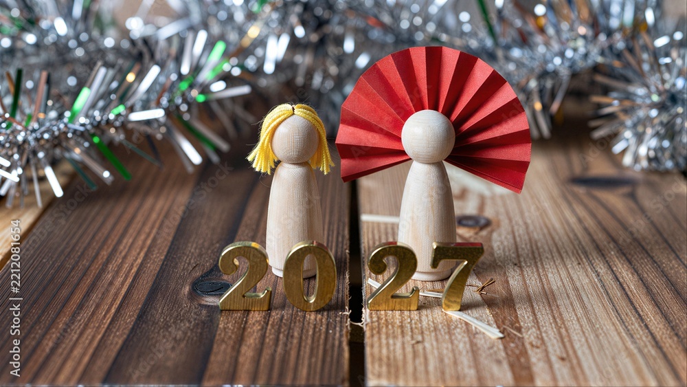 Fototapeta premium Wooden angels with red wings stand beside 2027 on a rustic wooden table.