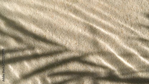 Slow motion water surface ripples and splash with palm tree leaf shadow on sand
