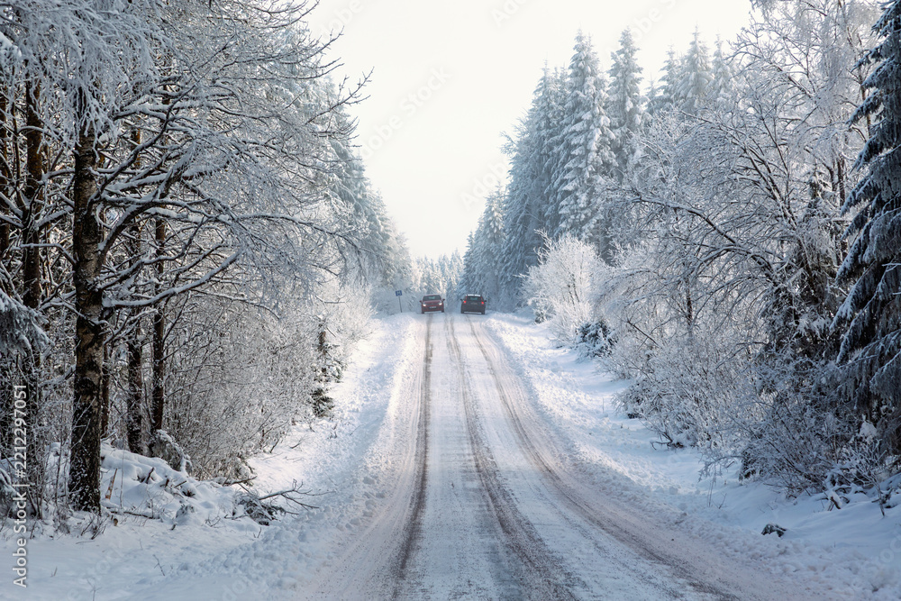 Fototapeta premium Two cars driving along a snow-covered road through a winter forest