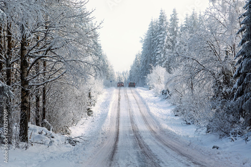 Two cars driving along a snow-covered road through a winter forest