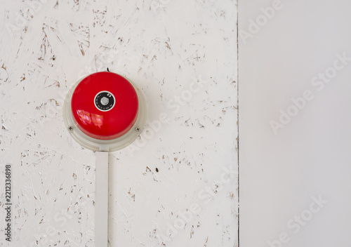 Red emergency fire alarm bell mounted on a white wall