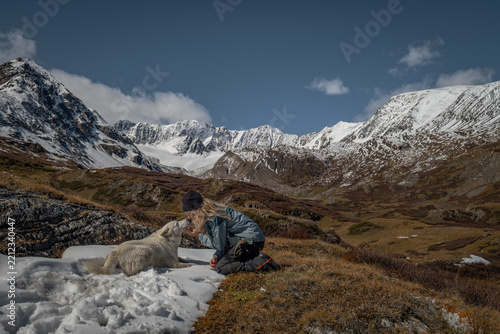 Fotografie Side view of a young female hiker petting her white dog on a snow patch against