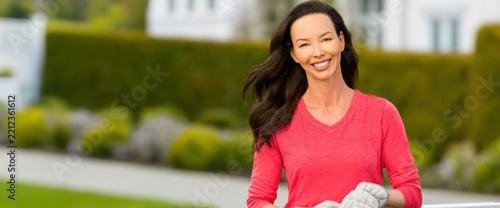 Woman smiling cheerfully while standing in a manicured garden outside her home.